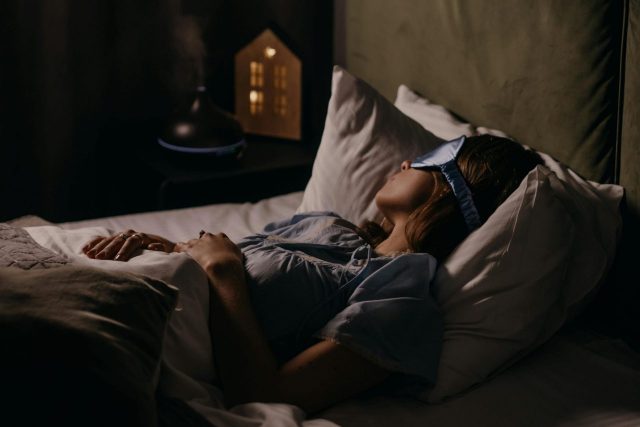 adult female sleeping soundly in bed wearing an eye mask in a dimly lit room
